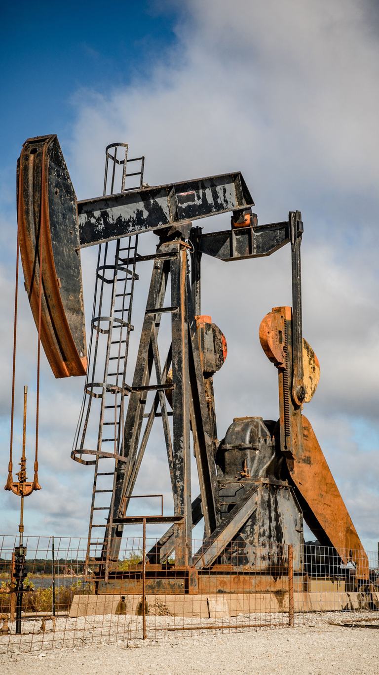 Rusted pumpjack at a producing well under a cloudy sky